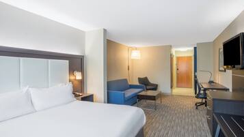 A hotel room with a bed, a desk, a chair, a sofa, and a television.