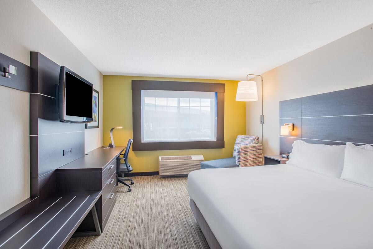 A hotel room with a bed, a desk, a chair, a TV, a window, and a lamp.