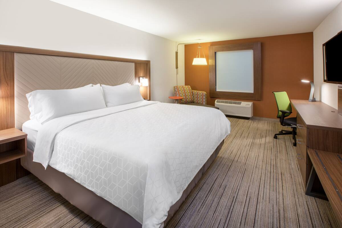 A hotel room with a large bed, a desk, a chair, a television, and a window.