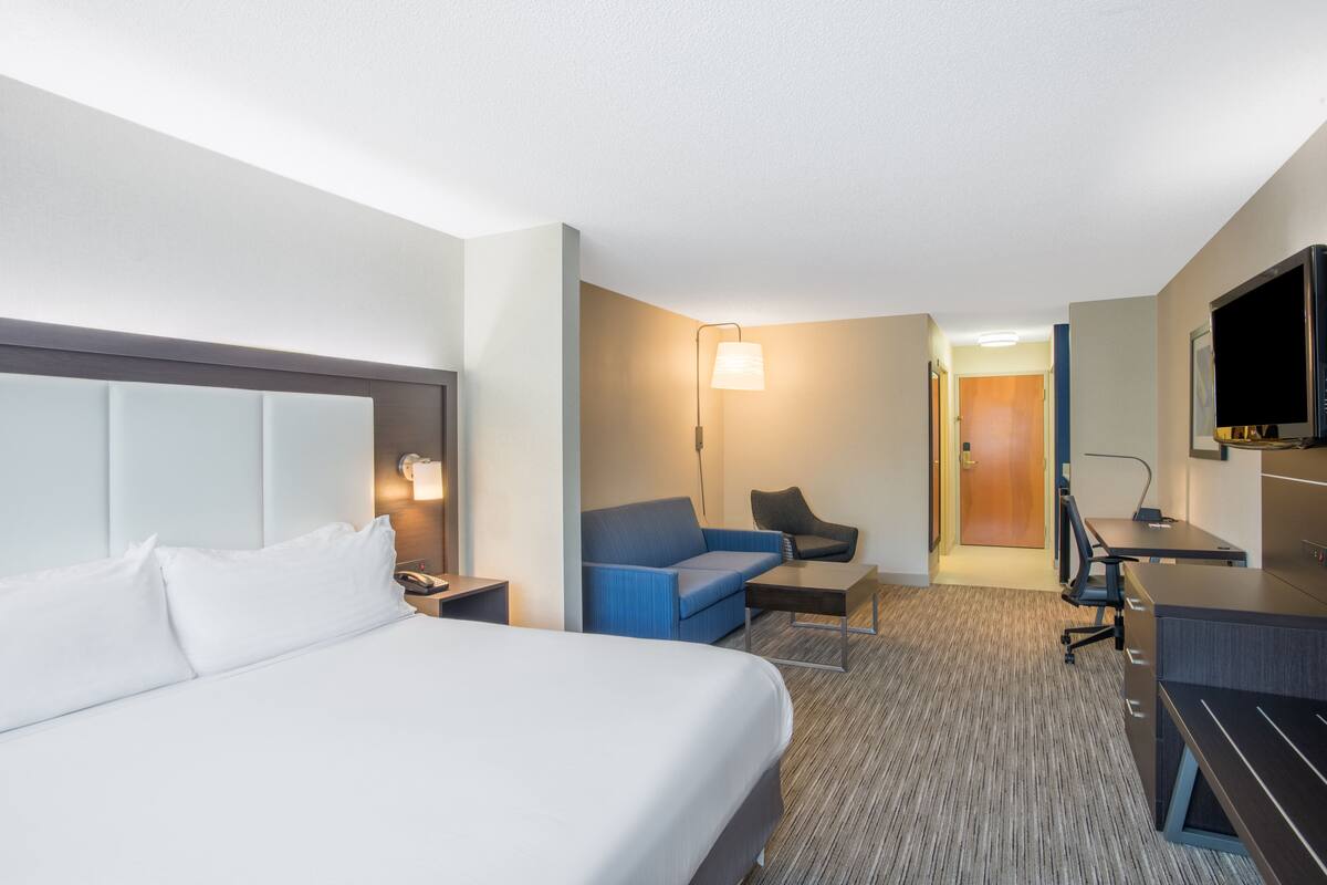 A hotel room with a large bed, a desk, a chair, a sofa, and a television.