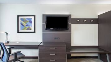A hotel room with a desk, chair, TV, and a framed picture on the wall.