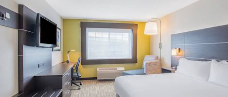 A hotel room with a bed, desk, chair, TV, window, and lamp.