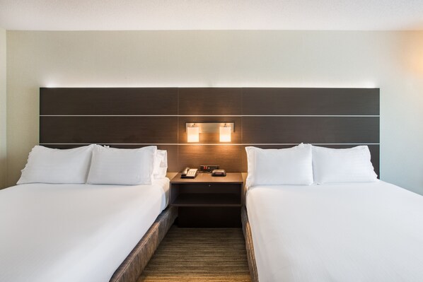 Habitación de hotel con dos camas, una mesita de noche con teléfono y reloj, y cabecera con iluminación integrada.