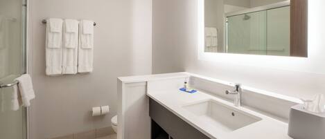 A modern bathroom with a glass shower enclosure, white towels, a large mirror, and a vanity with a sink.