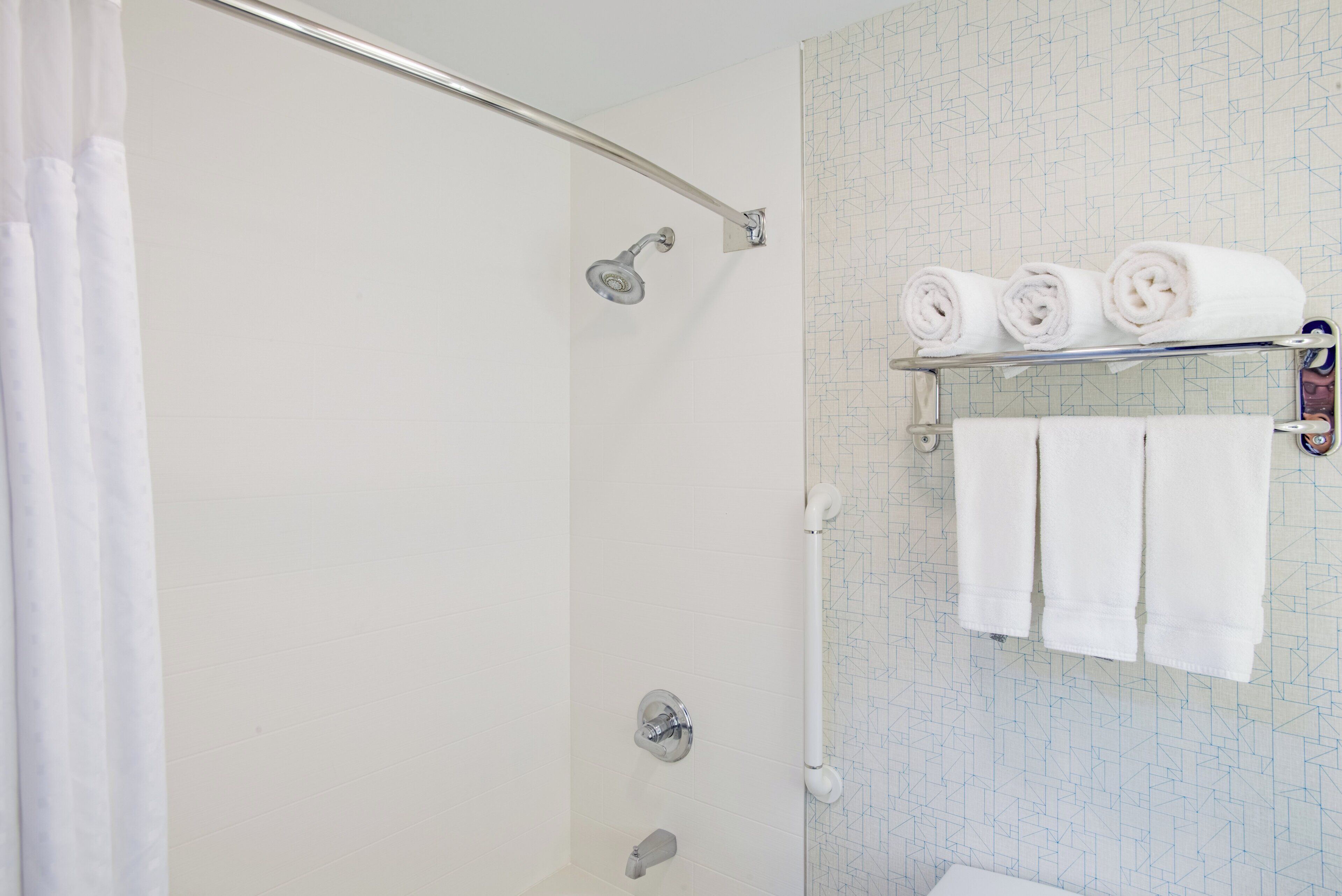 Une douche avec une porte en verre, un porte-serviettes avec des serviettes pliées et une pomme de douche.