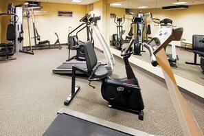 Un gimnasio con varios equipos de ejercicio, incluyendo cintas de correr, elípticas y máquinas de pesas.