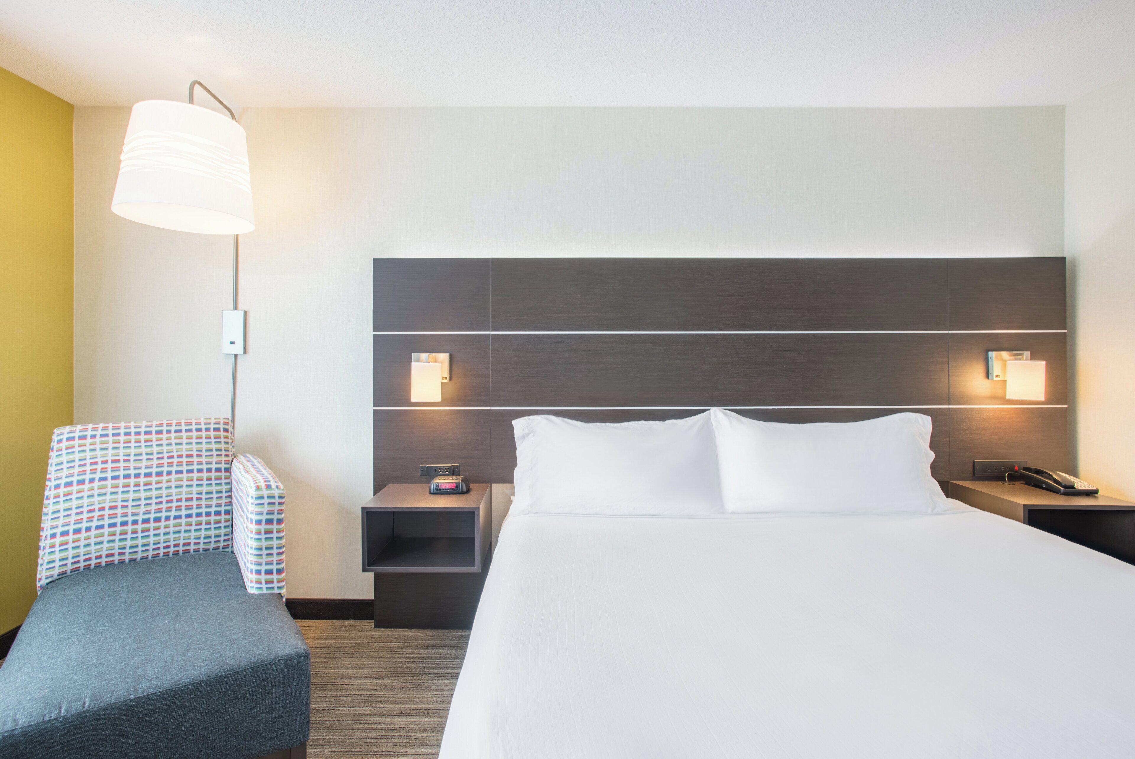 A hotel room with a bed, bedside tables, a lamp, a chair, and a carpeted floor.