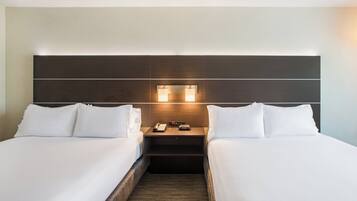 A hotel room with two single beds, a nightstand with a phone and a lamp, and a headboard with built-in lighting.
