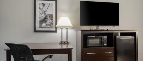 Ein Hotelzimmer mit Flachbildfernseher, Mikrowelle, Kühlschrank, Schreibtisch mit Stuhl und einem gerahmten Bild an der Wand.