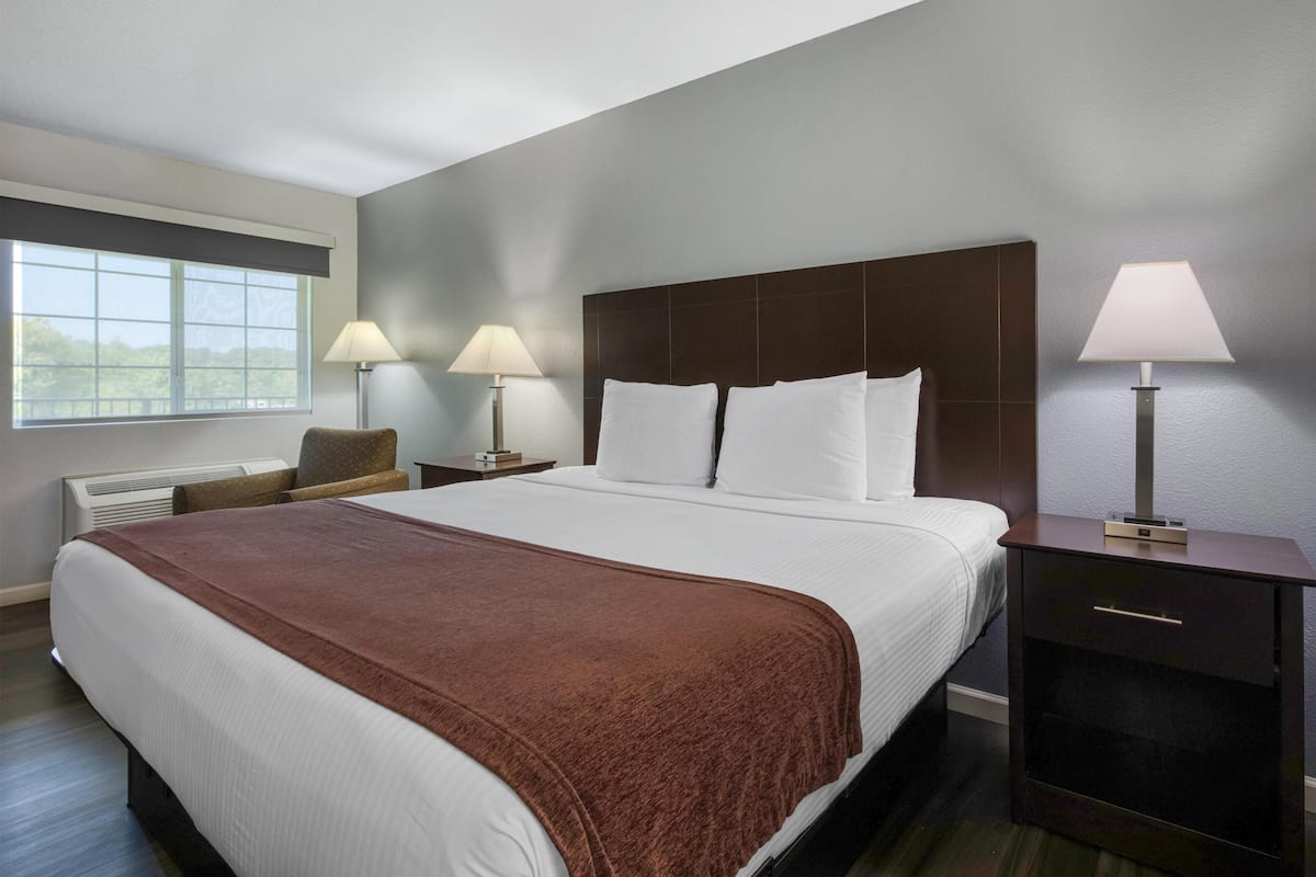 A hotel room with a large bed, two bedside tables with lamps, a chair, and a window with a view.