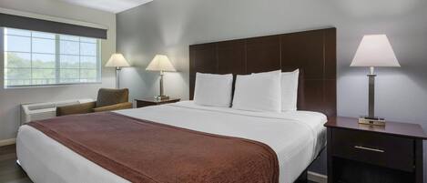 Habitación de hotel con una cama grande, dos mesitas de noche con lámparas, una silla y un ventanal con vistas.