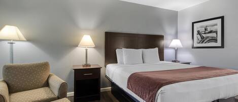 Une chambre d’hôtel avec un lit, deux lampes de chevet, une chaise, une table de chevet et un tableau encadré au mur.