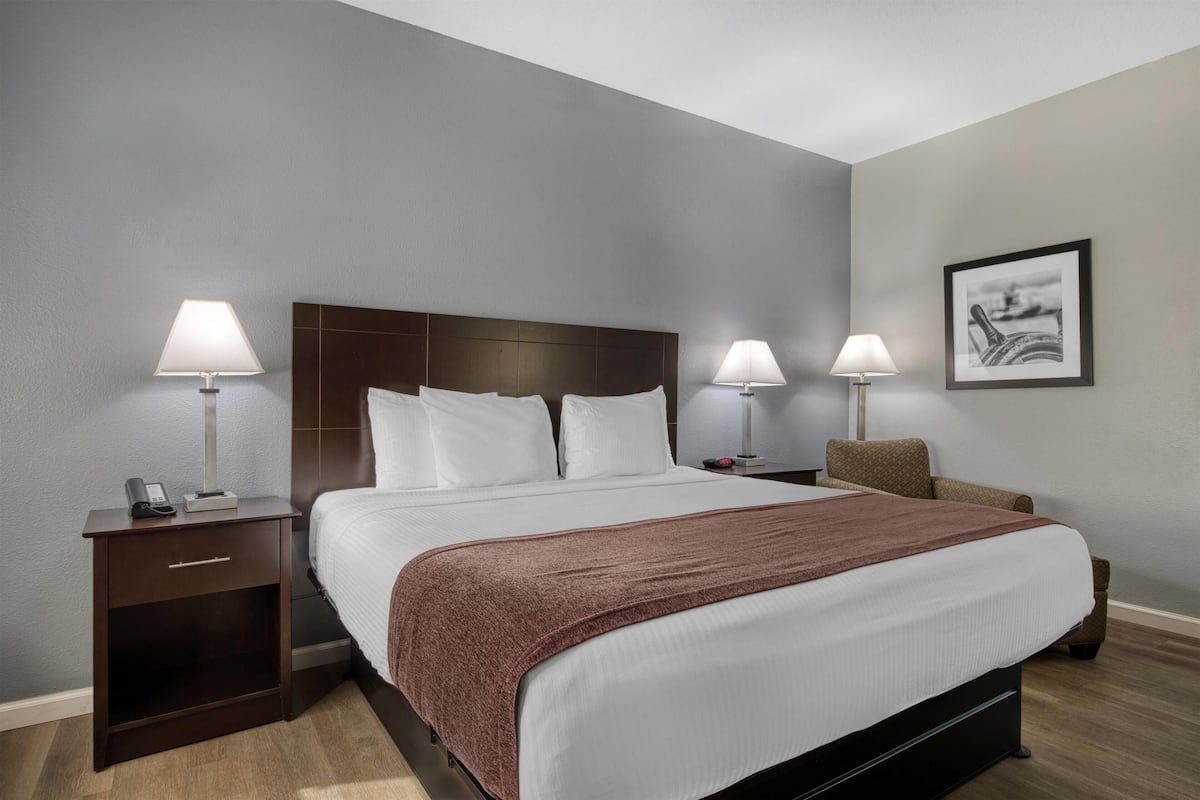 A hotel room with a large bed, two bedside tables, a chair, and a framed picture on the wall.