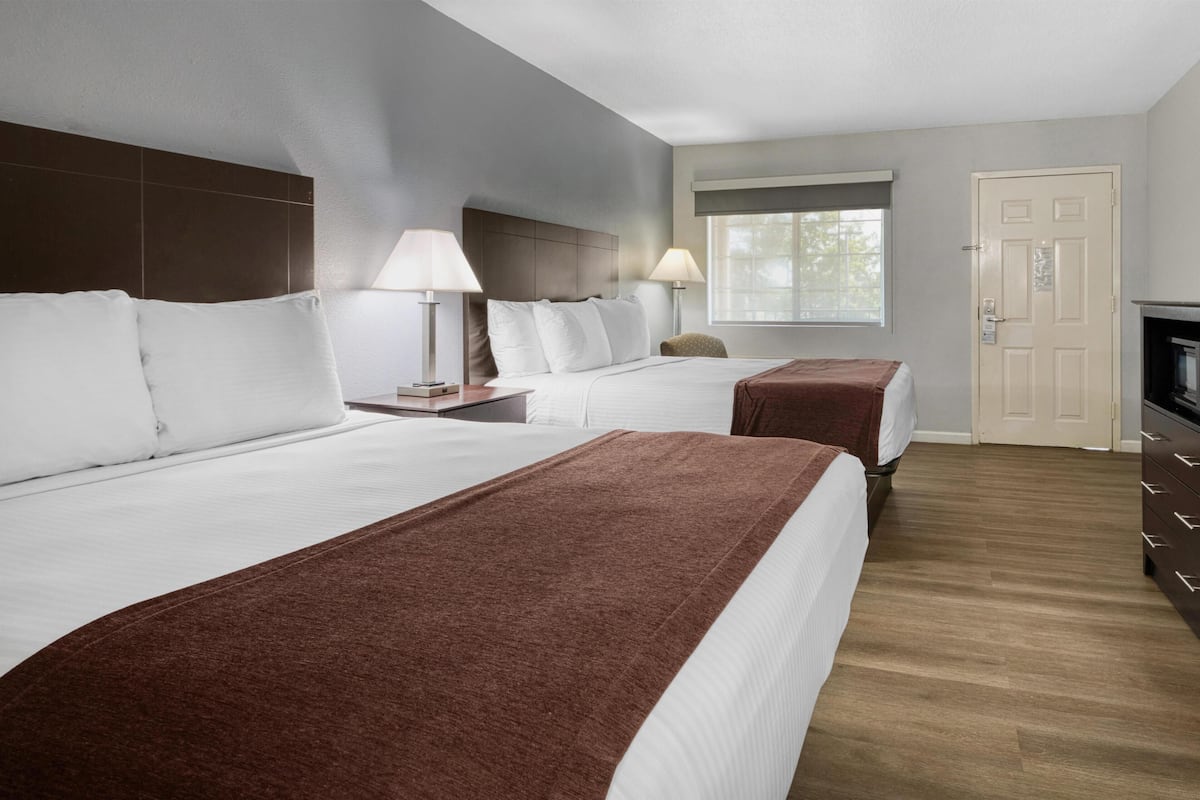 A hotel room with two beds, a window, a door, and a TV.
