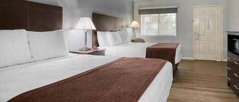 A hotel room with two beds, a window, a door, and a TV.