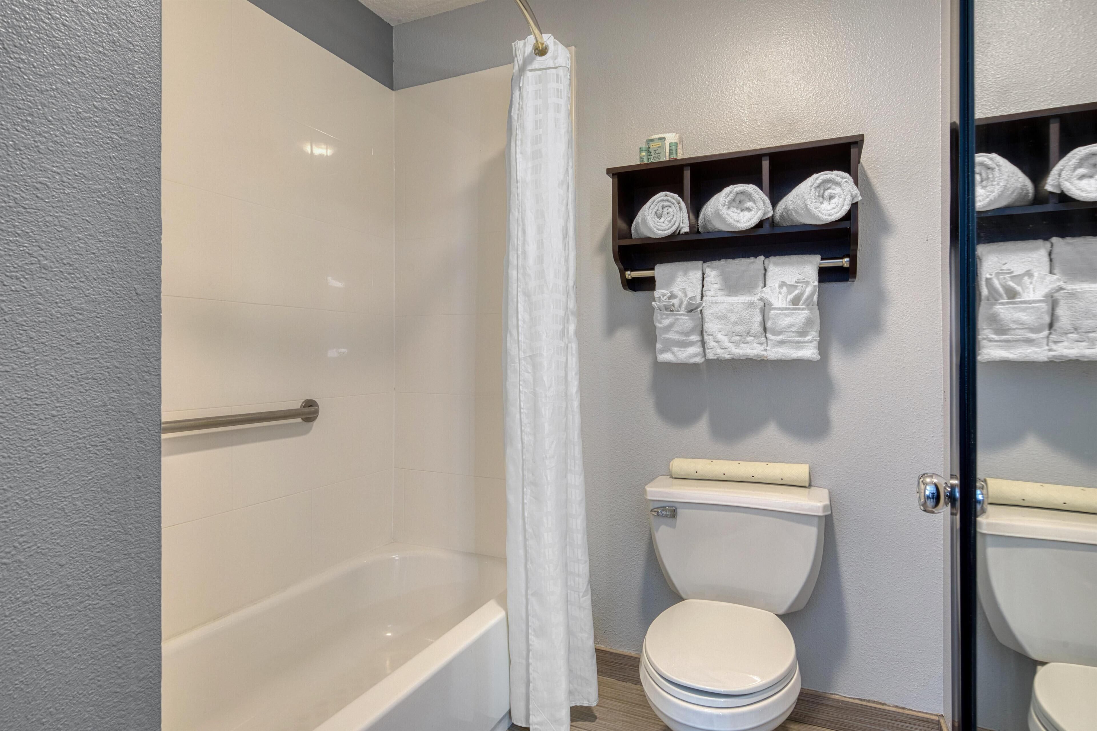 A bathroom with a bathtub, toilet, and a shelf with towels.