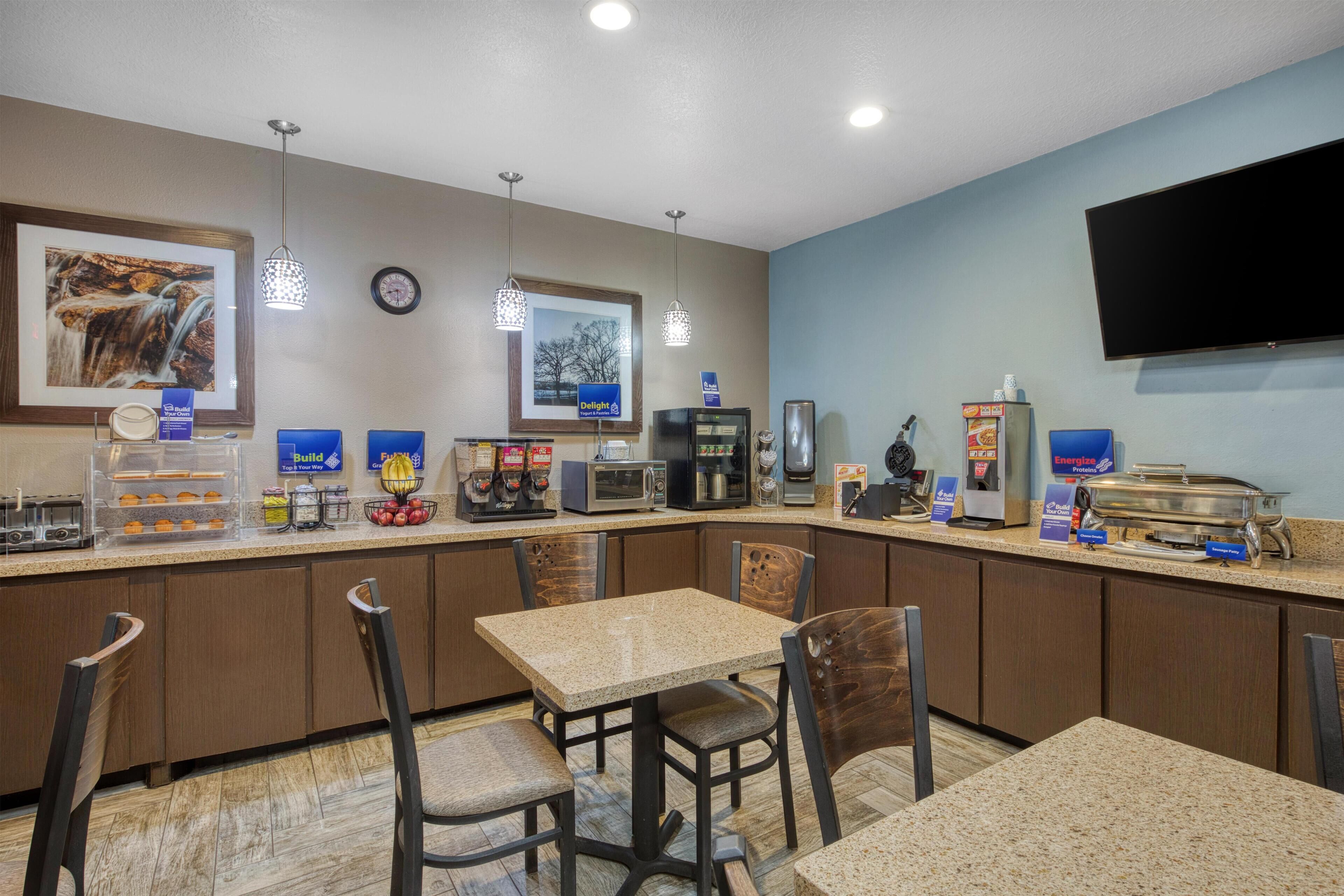 A hotel breakfast area with a counter, seating, and various food and beverage stations.