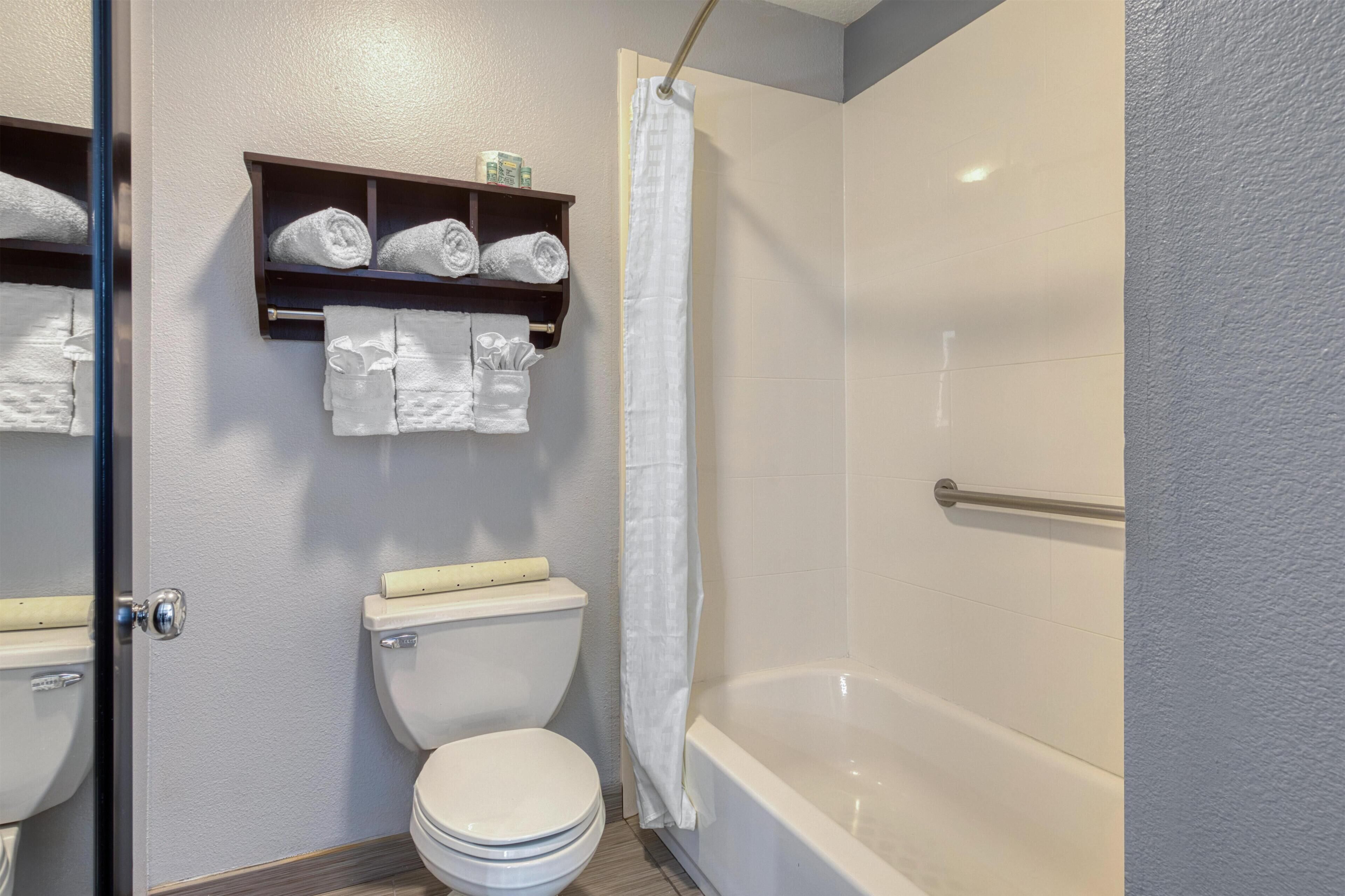 Un baño con inodoro, bañera y cortina de ducha. Hay toallas y artículos de aseo en un estante sobre el inodoro.