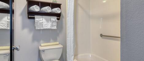 A bathroom with a toilet, a bathtub, and a shower curtain. There are towels and toiletries on a shelf above the toilet.
