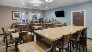 A hotel room with a large dining table, multiple chairs, a kitchen area with appliances, a flat-screen TV mounted on the wall, and a door with a sign. - Best Western Lake Conroe Inn (Montgomery)