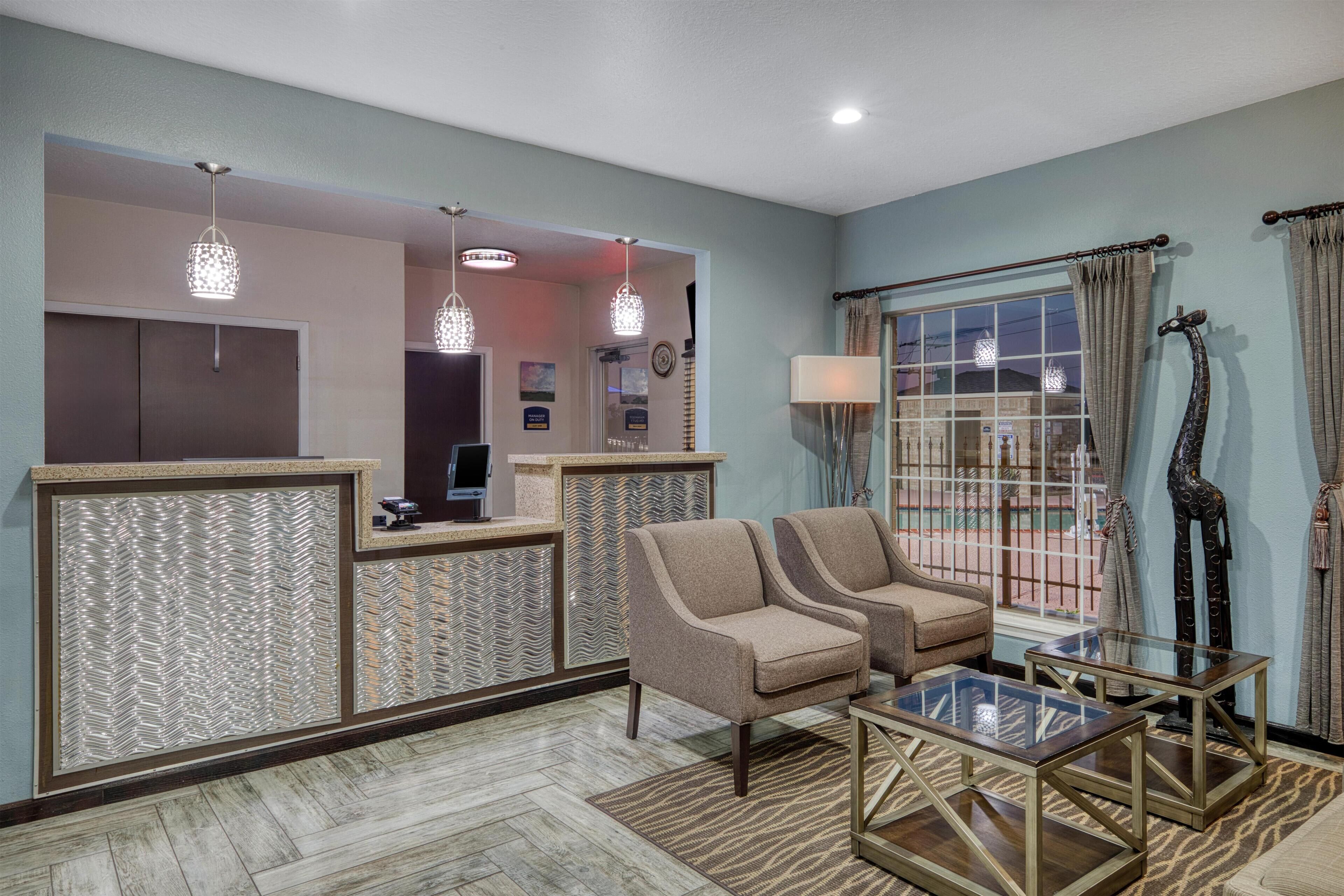 A reception area with a counter, two armchairs, a glass coffee table, and a large window with curtains.