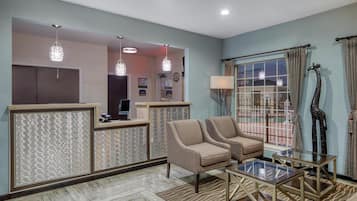 Un área de recepción con mostrador, dos sillones, una mesa de centro de vidrio y un amplio ventanal con cortinas.