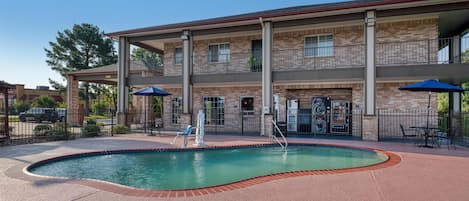 A two-story building with a swimming pool, outdoor seating, and a fenced patio area.
