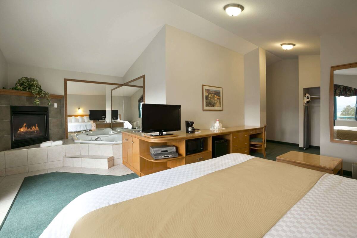 A hotel room with a large bed, a TV, a fireplace, a bathroom, and a desk.