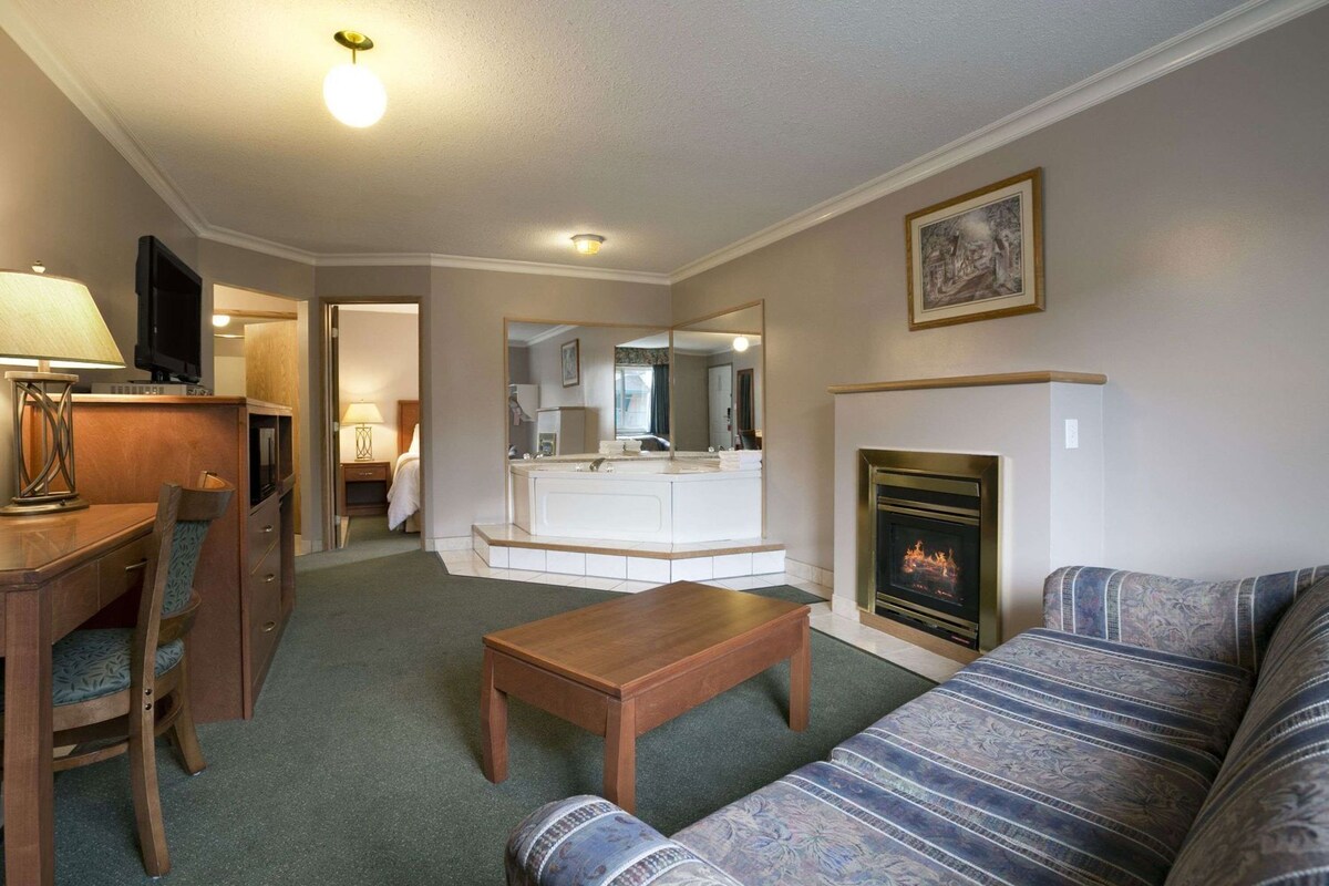 A hotel room with a living area, a dining area, a bathroom, and a fireplace.