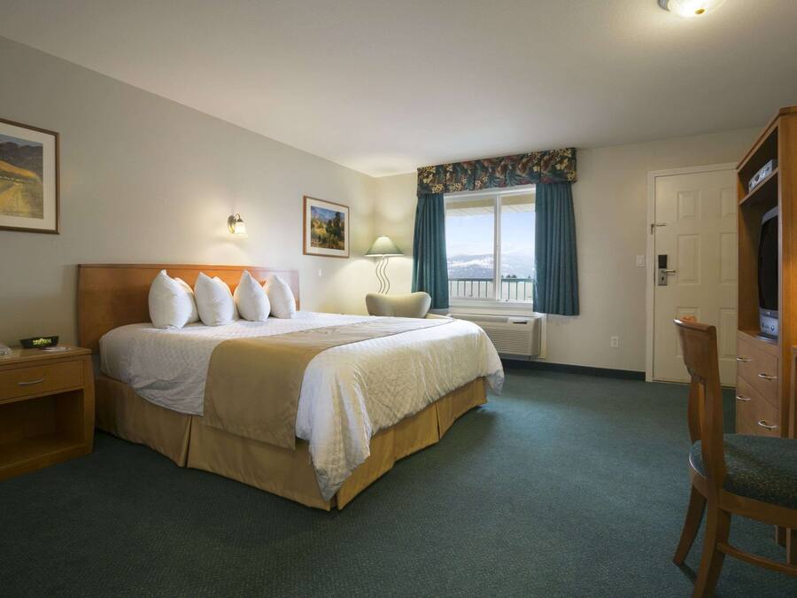 Ett hotellrum med en stor säng, ett skrivbord, en stol, ett nattduksbord, en lampa och ett fönster med utsikt.