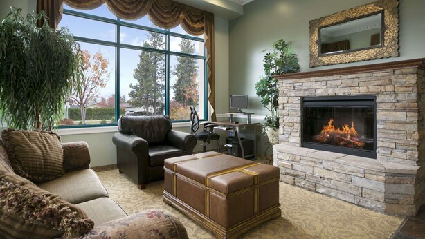 A living room with a stone fireplace, leather sofa, and a large window with curtains. - Ramada Limited Merritt (Merritt)