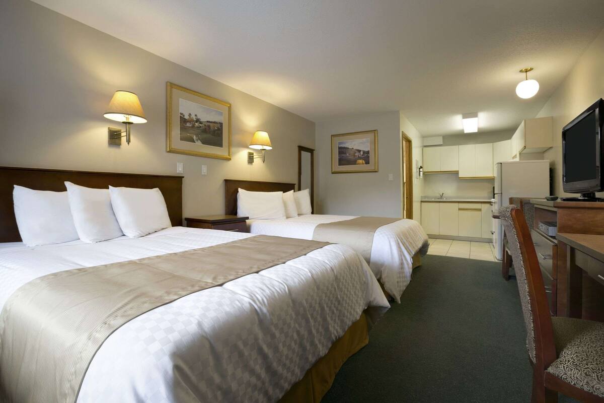 A hotel room with two beds, a desk with a chair, a television, and a kitchenette.