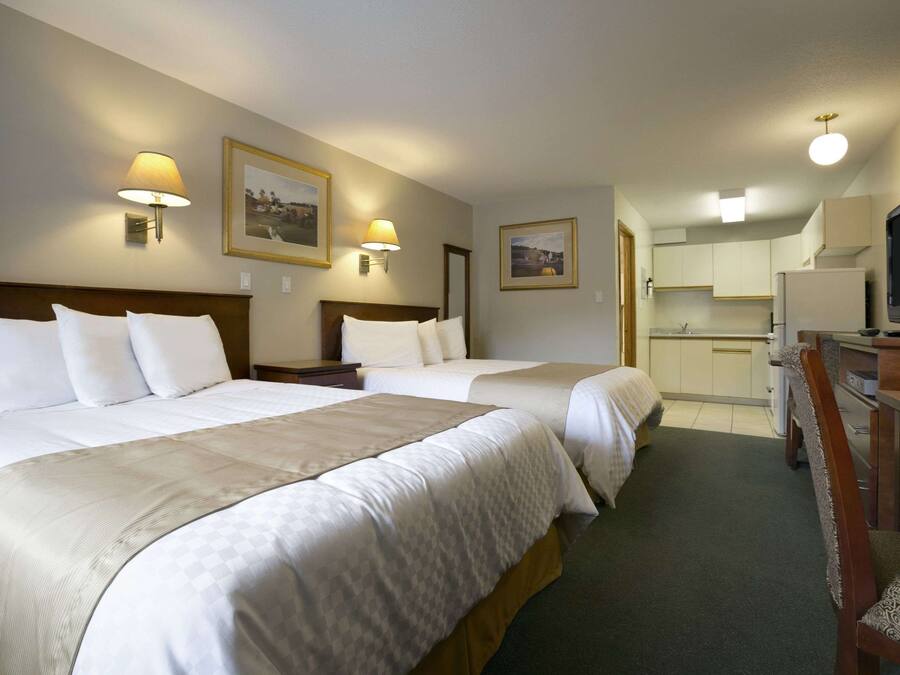 Et hotelværelse med to senge, et skrivebord med stol, et fjernsyn og et tekøkken.