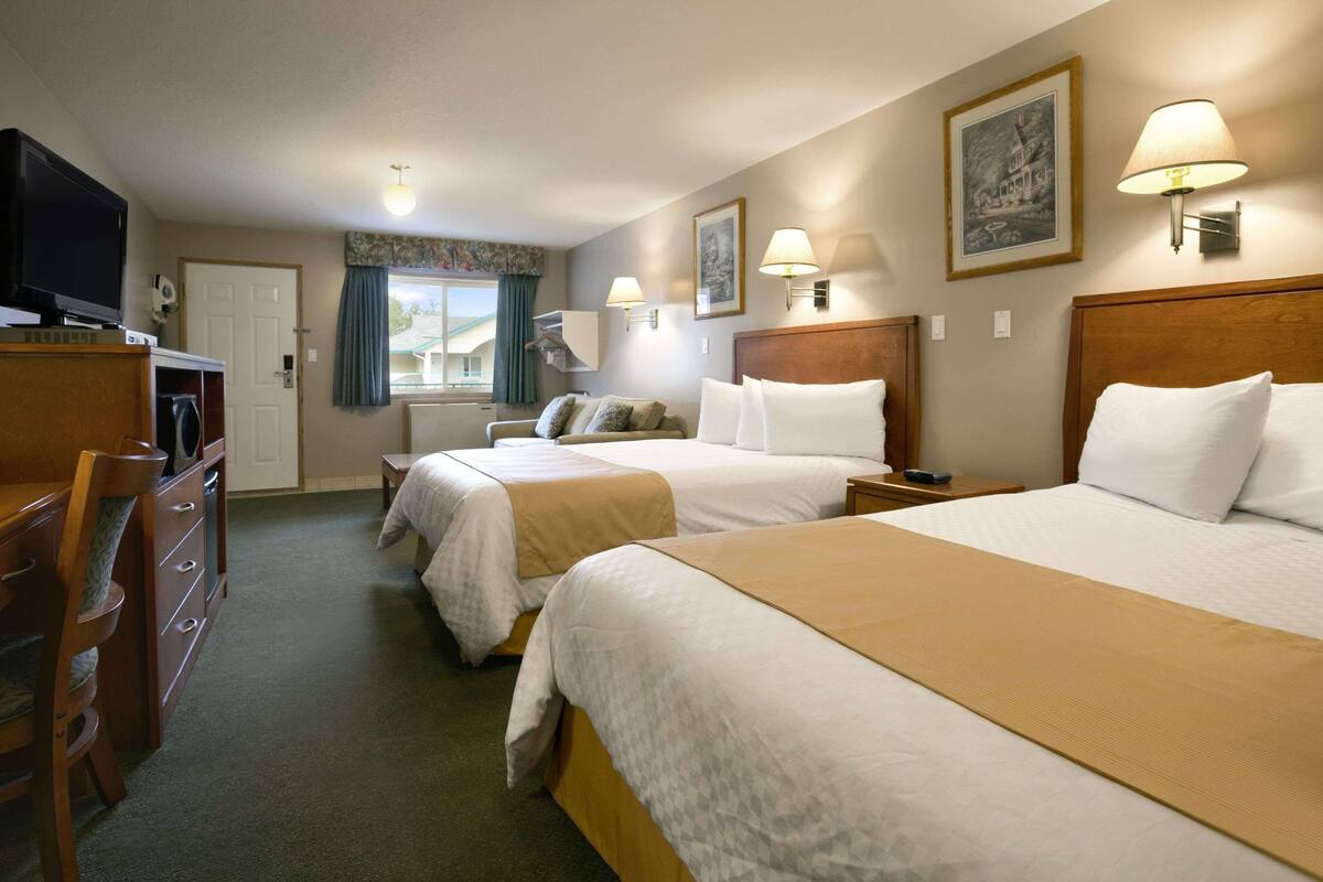 A hotel room with two beds, a TV, a desk, and a window with curtains.