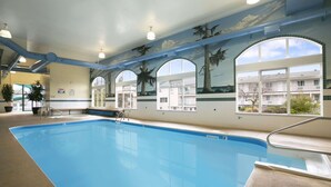 An indoor swimming pool with clear glass windows, a mural of palm trees, and a view of the outside buildings. - Ramada Limited Merritt (Merritt)
