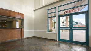 A lobby with a reception desk, a large window with a view of a water slide, and a door labeled "LOBBY". - Ramada Limited Merritt (Merritt)