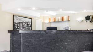 Un mostrador de recepción con fachada de piedra, un cartel de bienvenida enmarcado y un televisor montado.