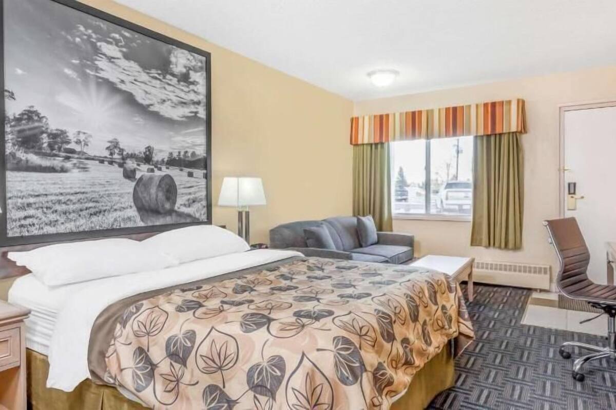 Hotelkamer met een bed, bureau, stoel, raam met gordijnen en een groot schilderij aan de muur.