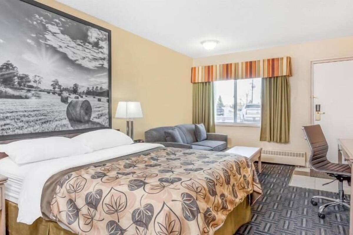 Een hotelkamer met een groot bed, een bureau, een stoel, een raam met gordijnen en een schilderij aan de muur.