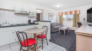 Habitación de hotel compacta con kitchenette, comedor con dos sillas, sofá, televisión y ventana con cortinas.