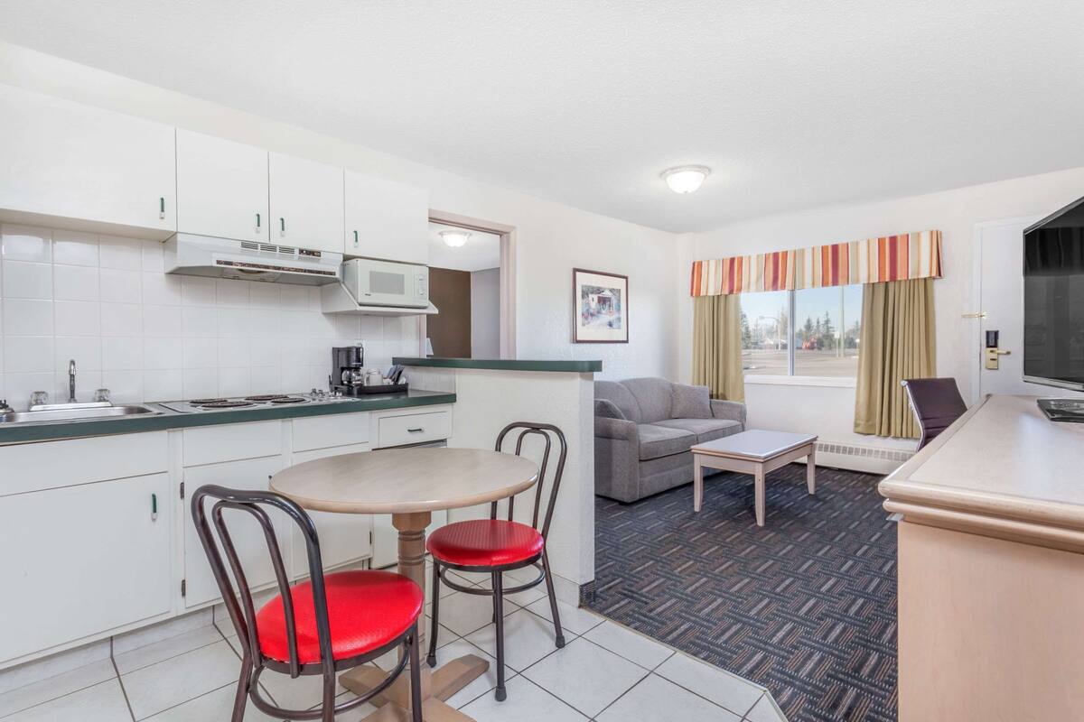 Een compacte hotelkamer met kitchenette, een zithoek met twee stoelen, een bank, een televisie en een raam met gordijnen.