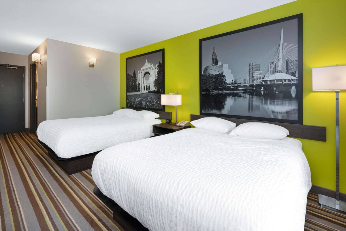 Una habitación de hotel con dos camas individuales, alfombra a rayas y dos lámparas de pared.