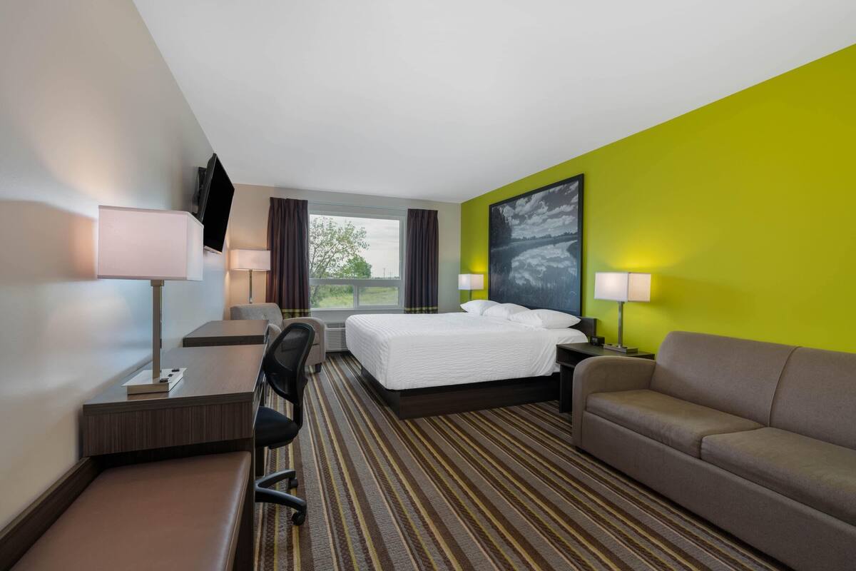 Una habitación de hotel con cama, escritorio, silla, sofá y un amplio ventanal.
