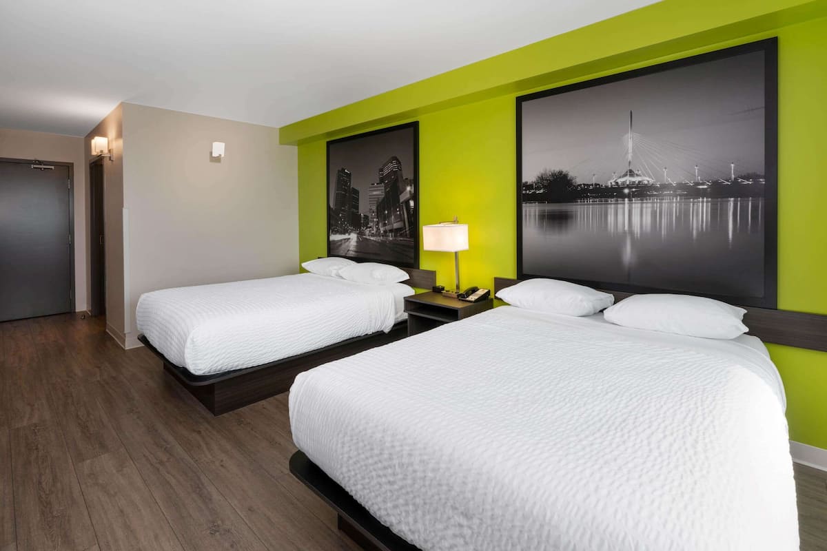 Habitación de hotel con dos camas, una mesita de noche con lámpara y dos cuadros en la pared.