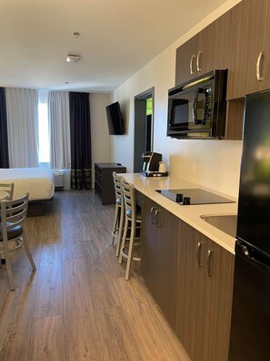Ein kompaktes Hotelzimmer mit Küchenzeile, einem Bett, einem Fernseher und einer Sitzecke.