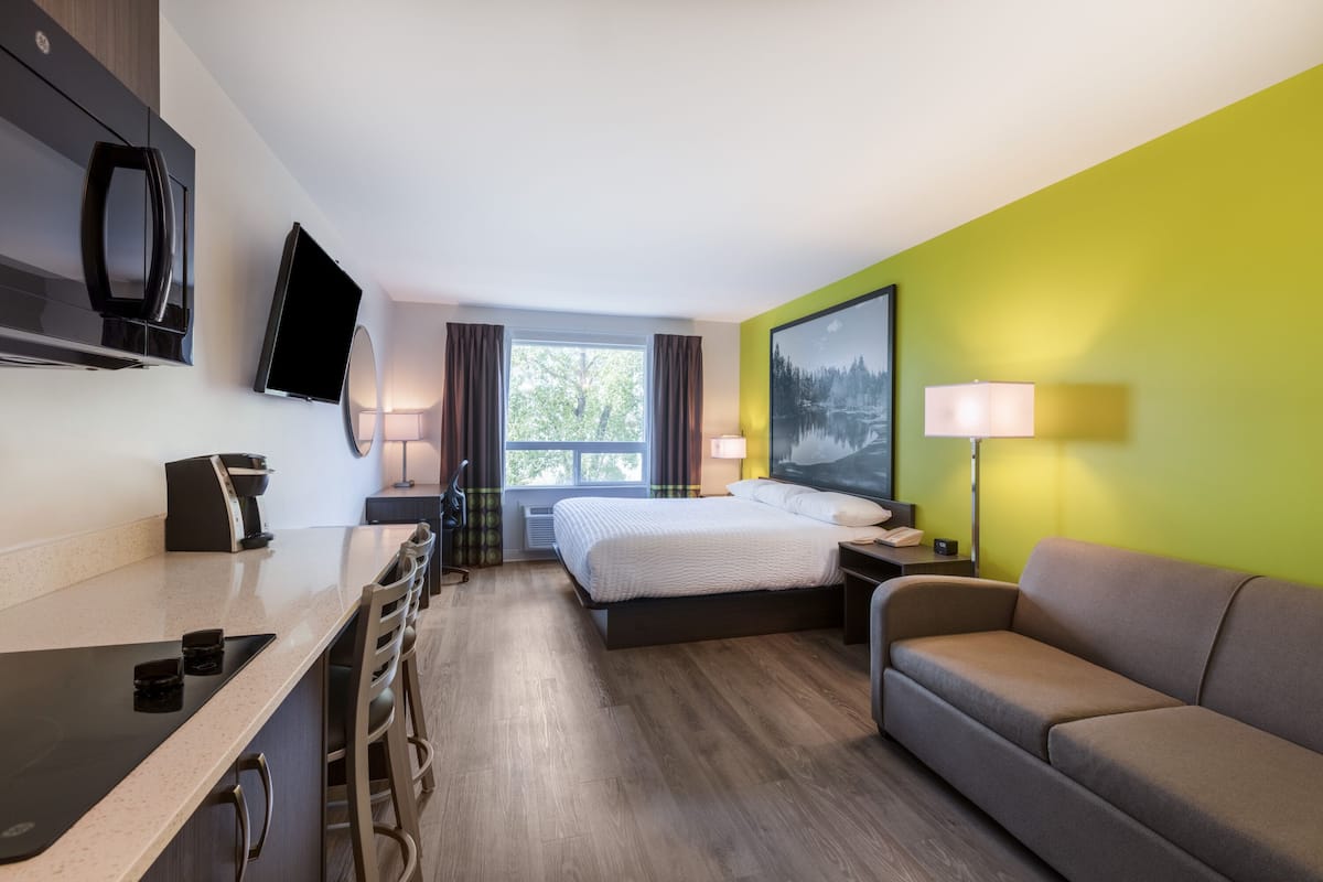 Una habitación de hotel moderna con una cama, un sofá, un escritorio con sillas, un televisor de pantalla plana y una ventana con cortinas.