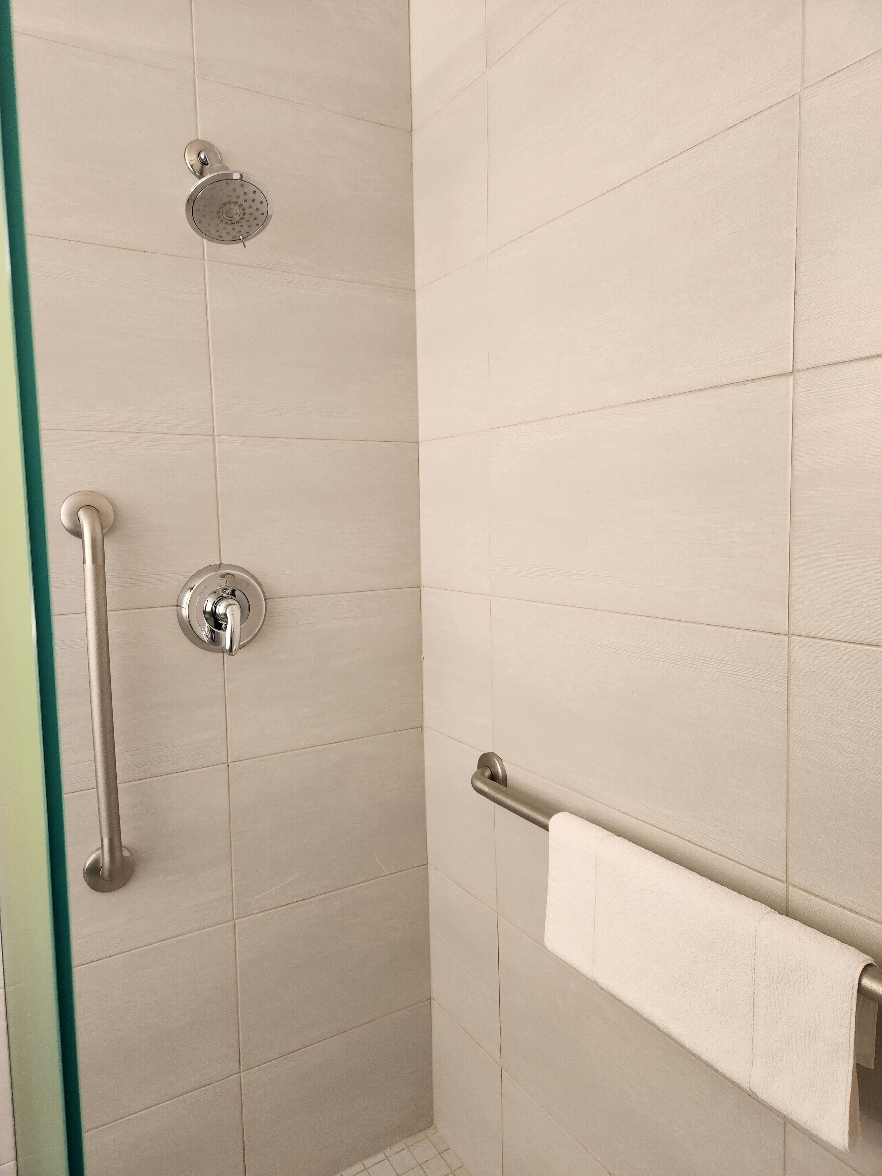 Ducha con cabezal de ducha de mano, control de ducha manual y barra de toallas con una toalla.