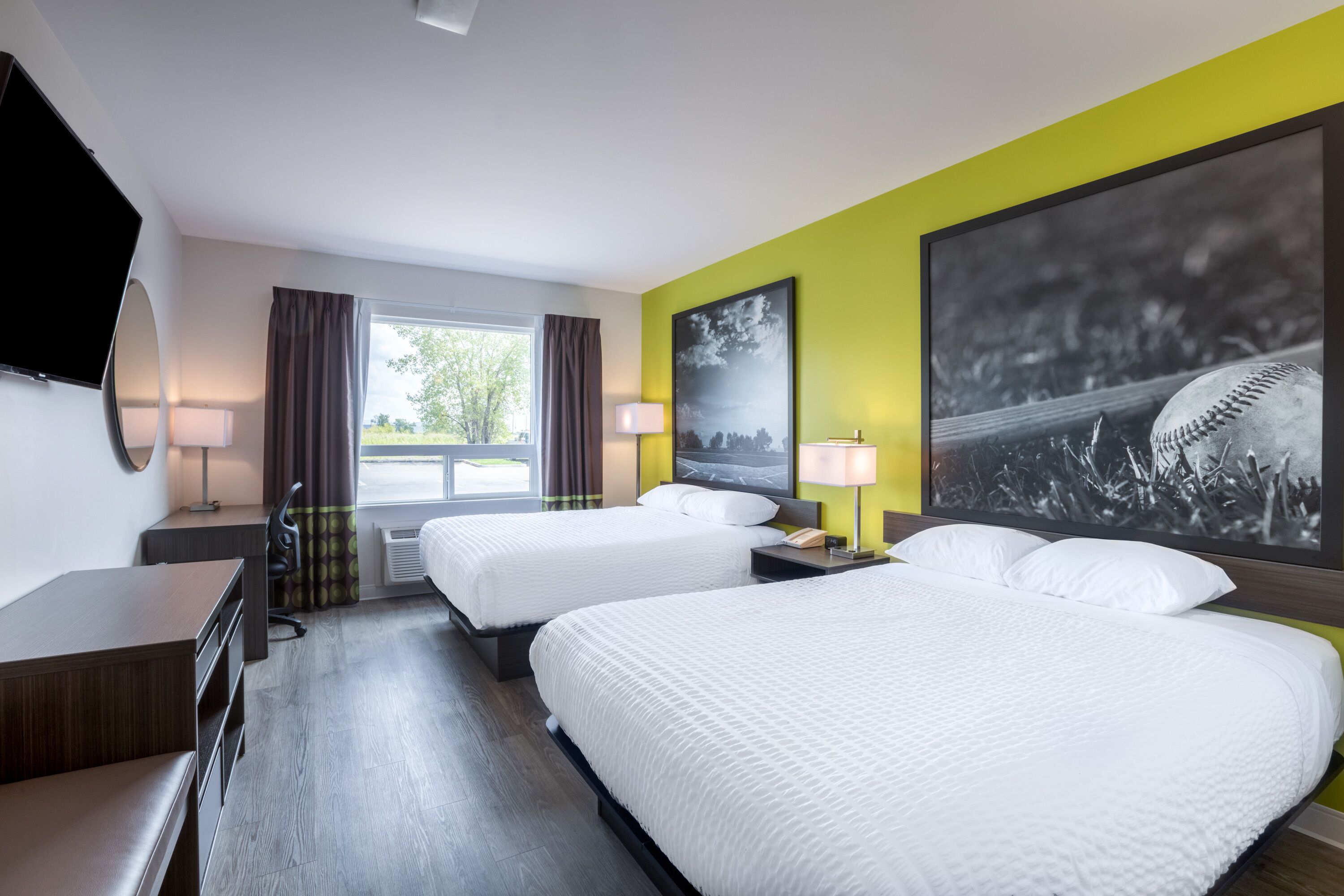A hotel room with two beds, a desk, a chair, a TV, and a window with curtains.