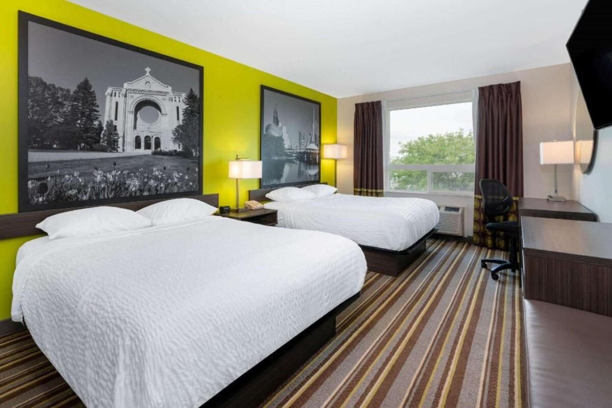 Ein Hotelzimmer mit zwei Betten, einem Schreibtisch, einem Stuhl und einem großen Fenster.