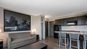 A modern kitchen with a microwave, refrigerator, and bar stools. There is a sofa and a coffee table in the living area, and a cityscape painting on the wall. - Super 8 by Wyndham Winnipeg East MB (Winnipeg)